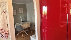 Une cuisine moderne avec des meubles rouges, un plan de travail blanc et un coin repas visible à travers une arche.