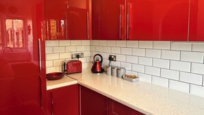 Une cuisine moderne avec des armoires rouges, des carreaux de céramique blancs de type « métro » et des appareils électroménagers en acier inoxydable.