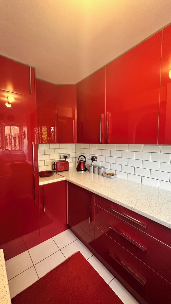 A modern kitchen with red cabinets, white subway tiles, and stainless steel appliances.
