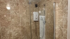 Une douche à l’italienne avec une porte en verre, une douchette à main et un panneau de commande.