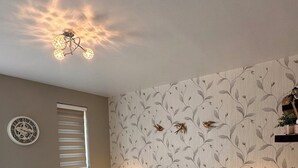Une chambre à coucher avec une couvre-lit à motifs floraux, une horloge au mur et une fenêtre avec des stores.