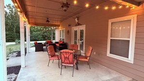 A covered patio area with outdoor furniture, string lights, and a ceiling fan.