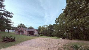 A house with a covered porch, a gravel driveway, and surrounding trees.