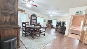 A spacious living area with a dining table, chairs, a ceiling fan, a bookshelf, and a television.