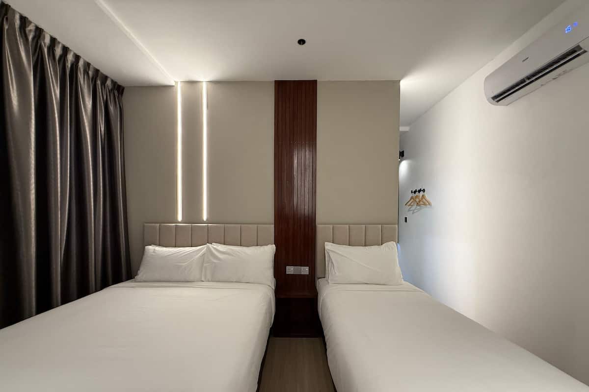 Habitación de hotel con dos camas individuales, un panel de pared de madera, un equipo de aire acondicionado y una cortina a la izquierda.
