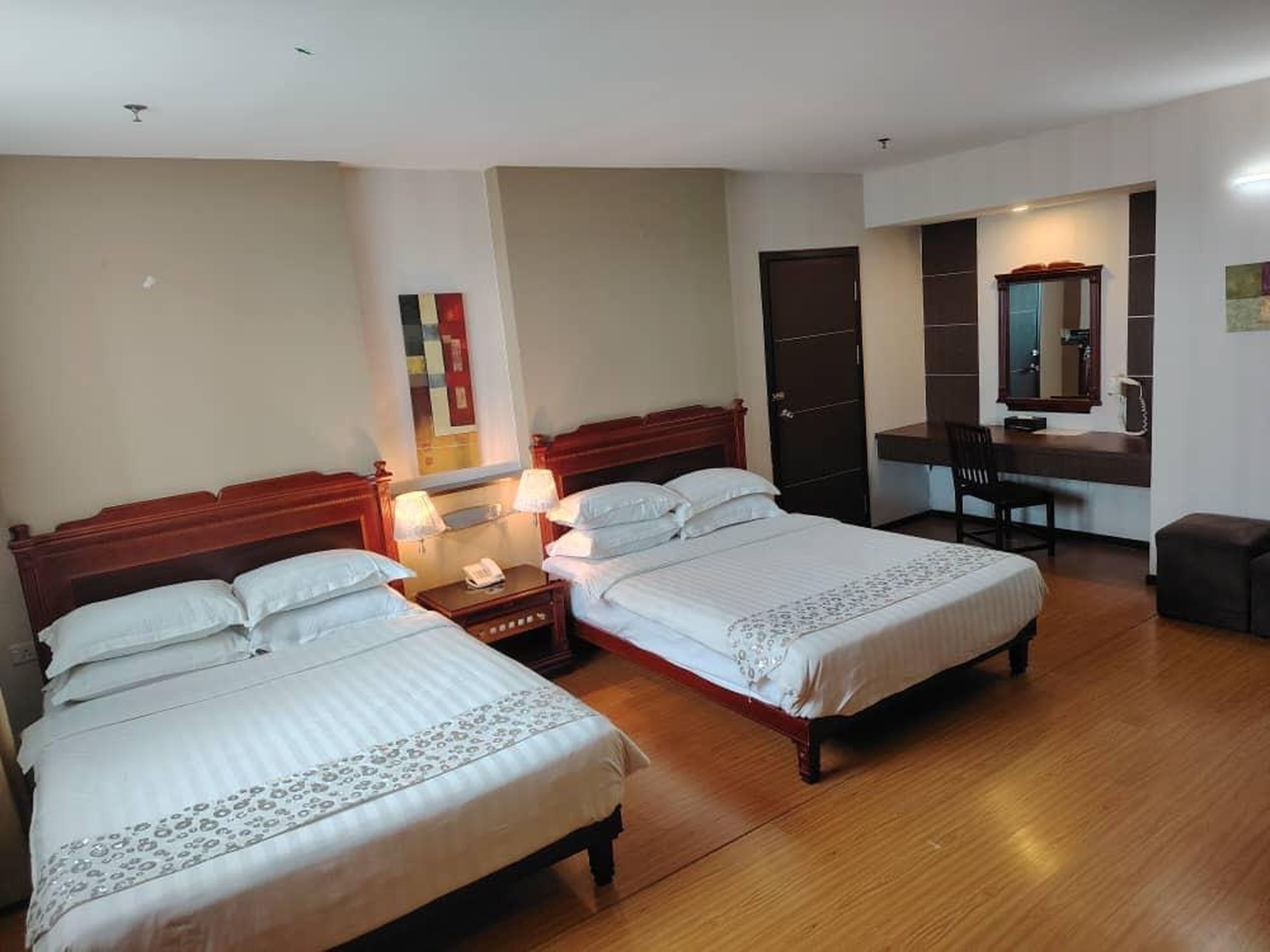 Una habitación de hotel con dos camas individuales, un escritorio con silla, un espejo y una puerta.