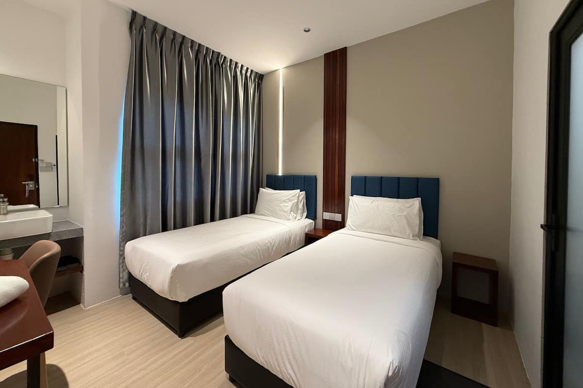 Habitación de hotel con dos camas individuales, un escritorio, una silla, un espejo y un ventanal grande con cortinas.