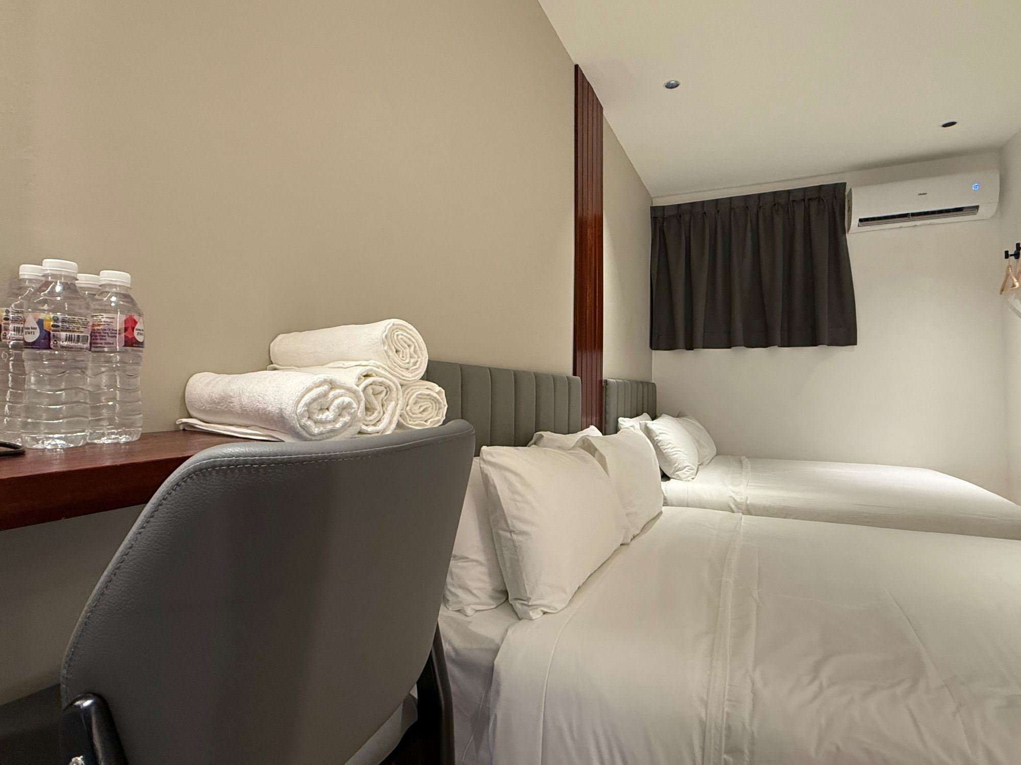 Una camera d'albergo con un letto, una scrivania con bottiglie d'acqua e asciugamani, e un condizionatore d'aria.