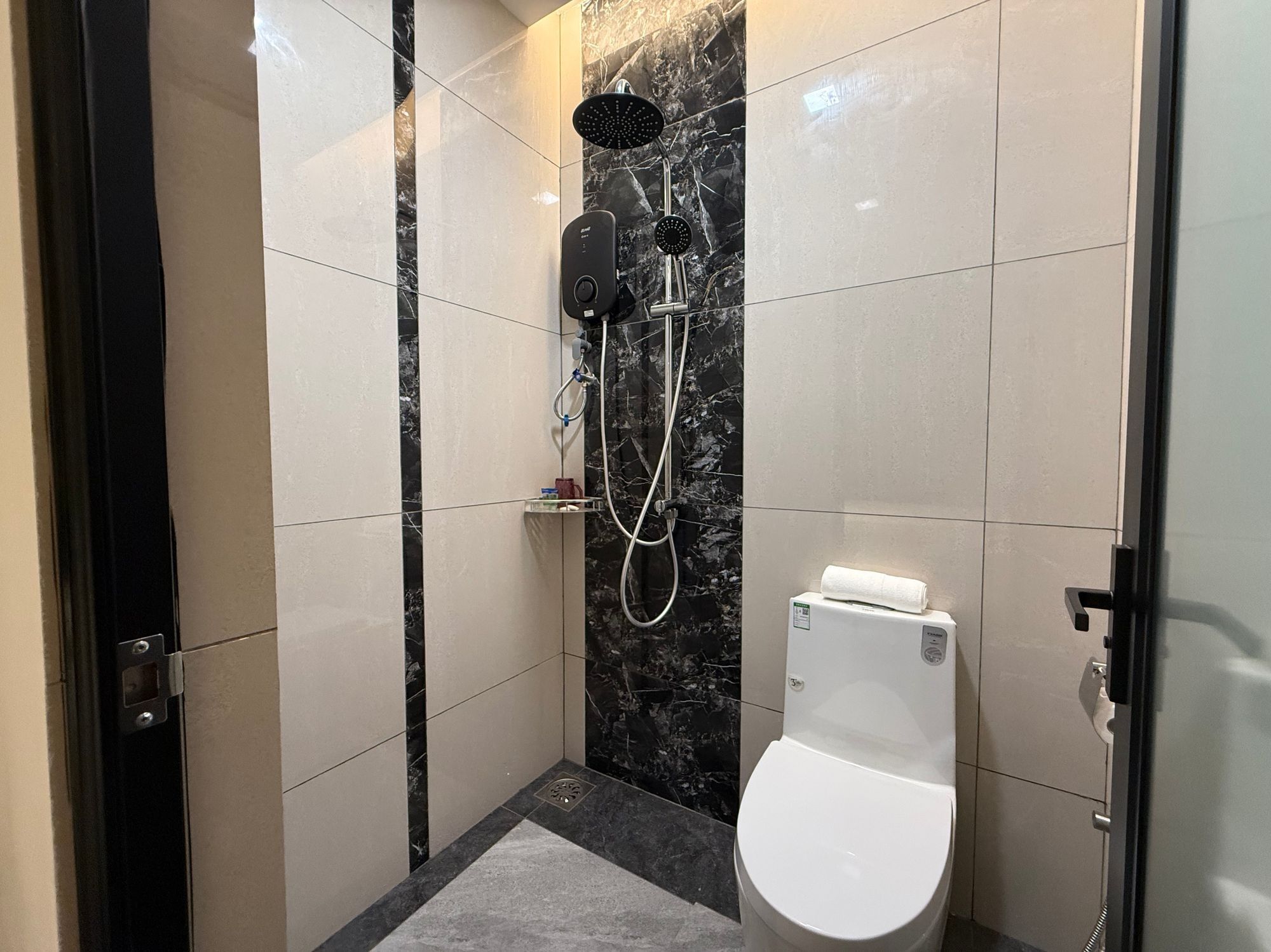 Een moderne badkamer met een douche, toilet en marmeren wanden.