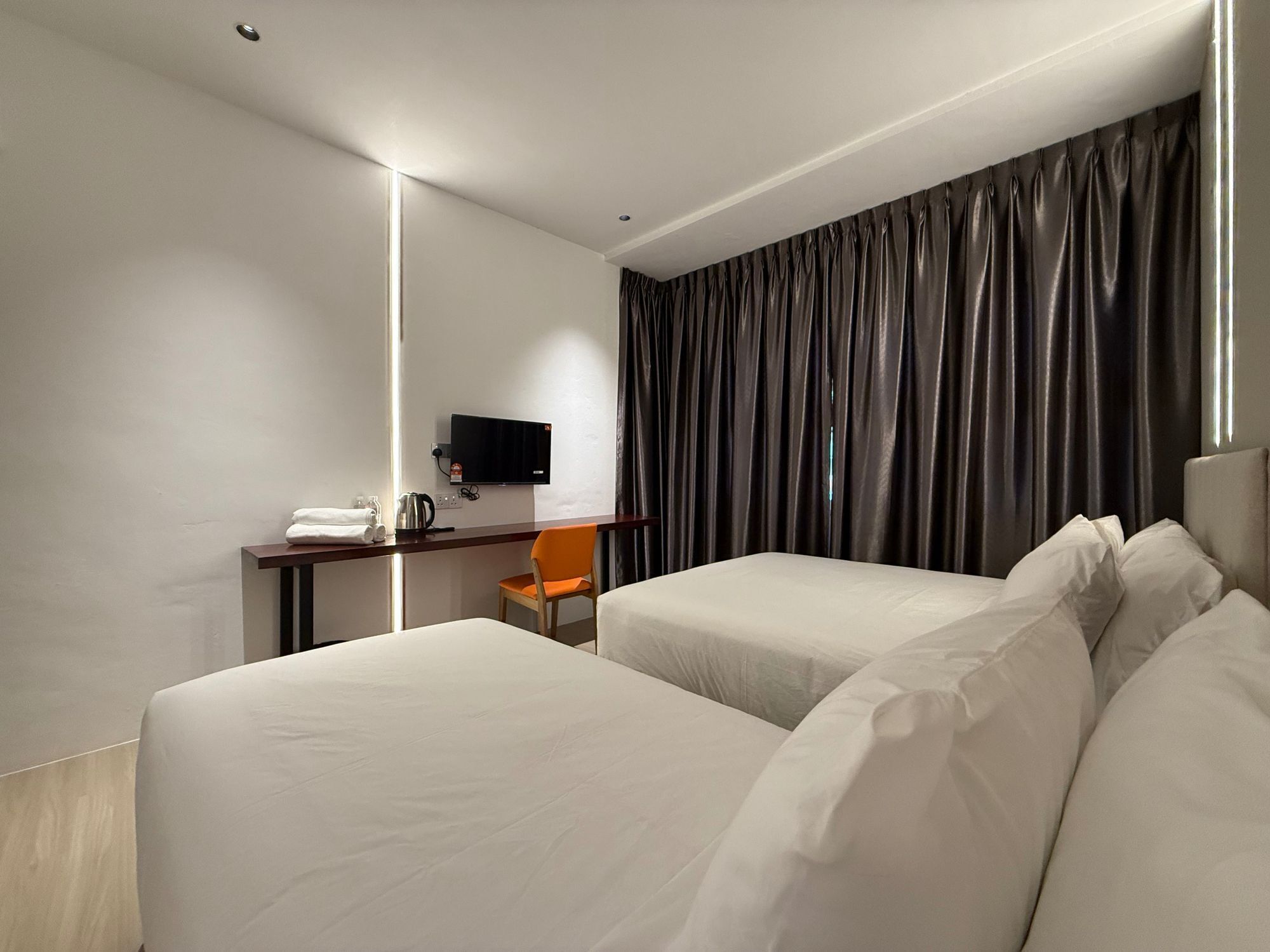 Ein Hotelzimmer mit zwei Betten, einem Schreibtisch, einem Flachbildfernseher, einem Stuhl und einem großen Fenster mit Vorhängen.