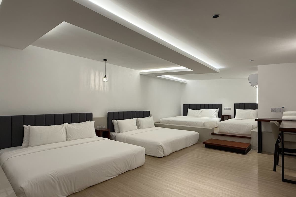 Una habitación de hotel moderna con tres camas, un escritorio y una pequeña zona de estar.
