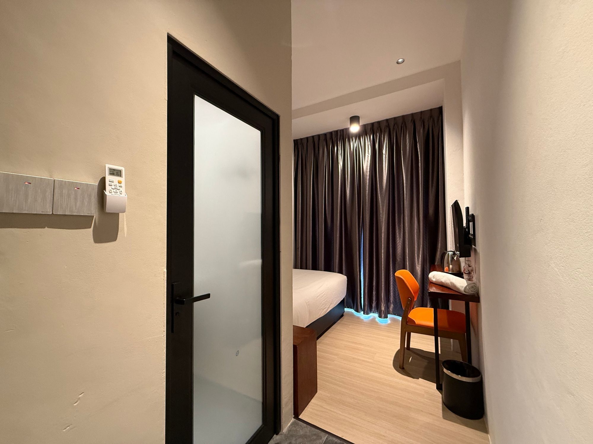 Habitación de hotel con una cama, un escritorio con una silla, una mesita con una botella y un cubo de basura.