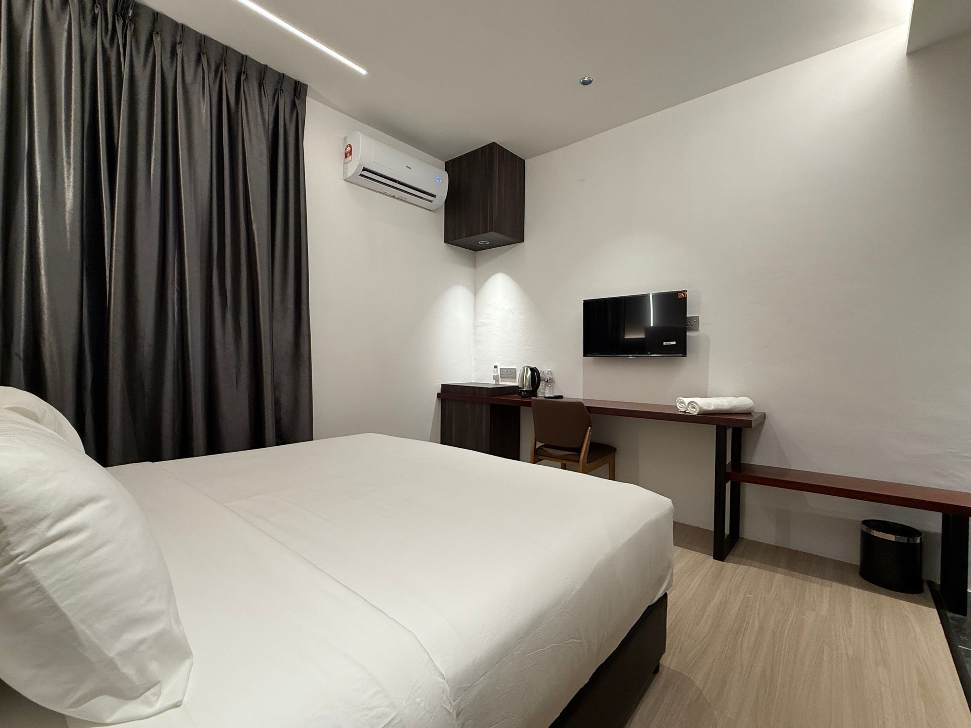 A hotel room with a bed, a desk with a chair, a television, and an air conditioning unit.