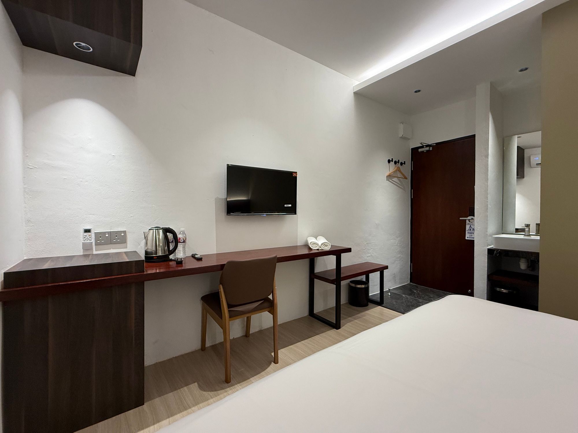 Habitación de hotel con cama, escritorio con silla, televisión, cafetera y una mesita con toallas.