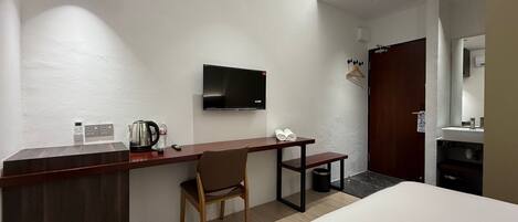 Habitación de hotel con cama, escritorio con silla, televisión, cafetera y una mesita con toallas.