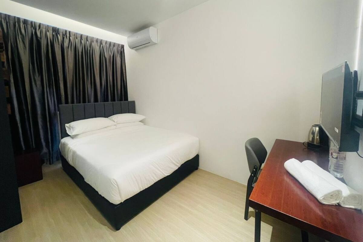 Habitación de hotel con cama, escritorio con televisor, silla y aire acondicionado.