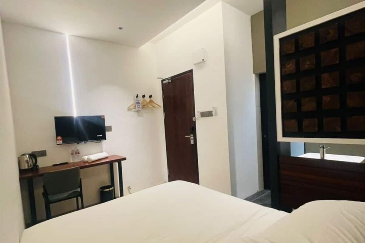 Una habitación de hotel con cama, escritorio con silla, televisor y baño con espejo.
