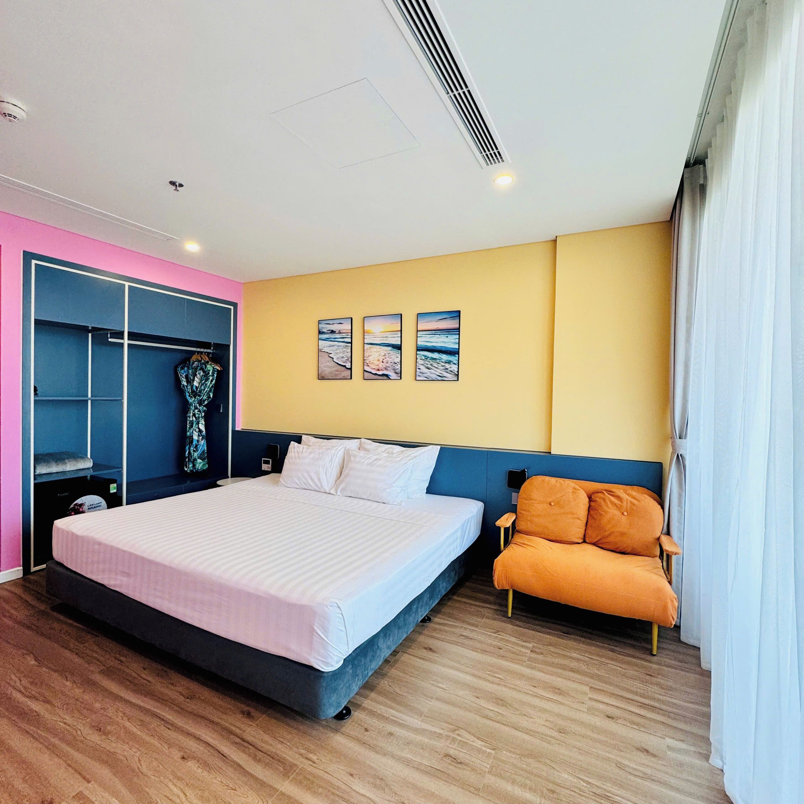 A hotel room with a bed, a chair, a wardrobe, and three wall-mounted pictures.