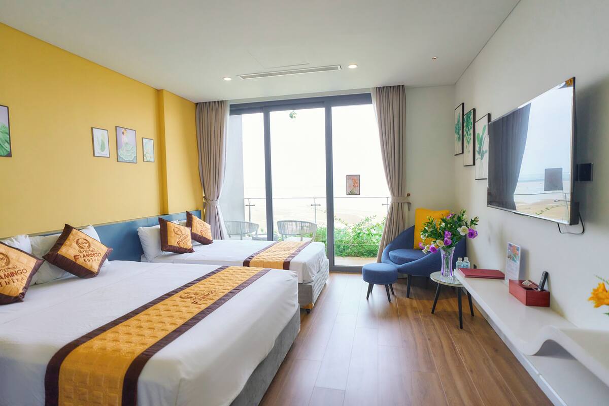 A hotel room with two beds, a balcony, a TV, and a small table with a vase of flowers.