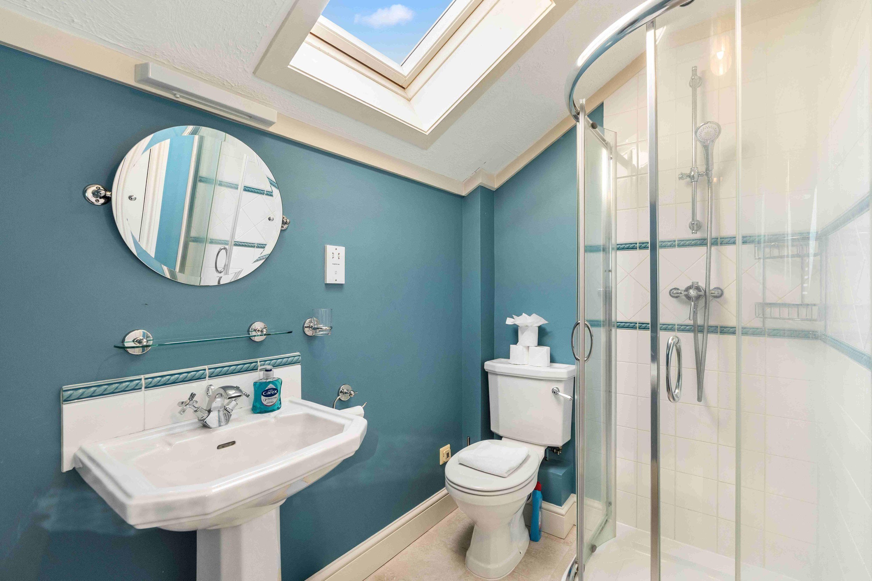Une salle de bain dotée d’un puits de lumière, d’un lavabo, de toilettes et d’une cabine de douche en verre.