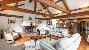 A spacious living room with a fireplace, wooden beams, and a staircase leading to another level.