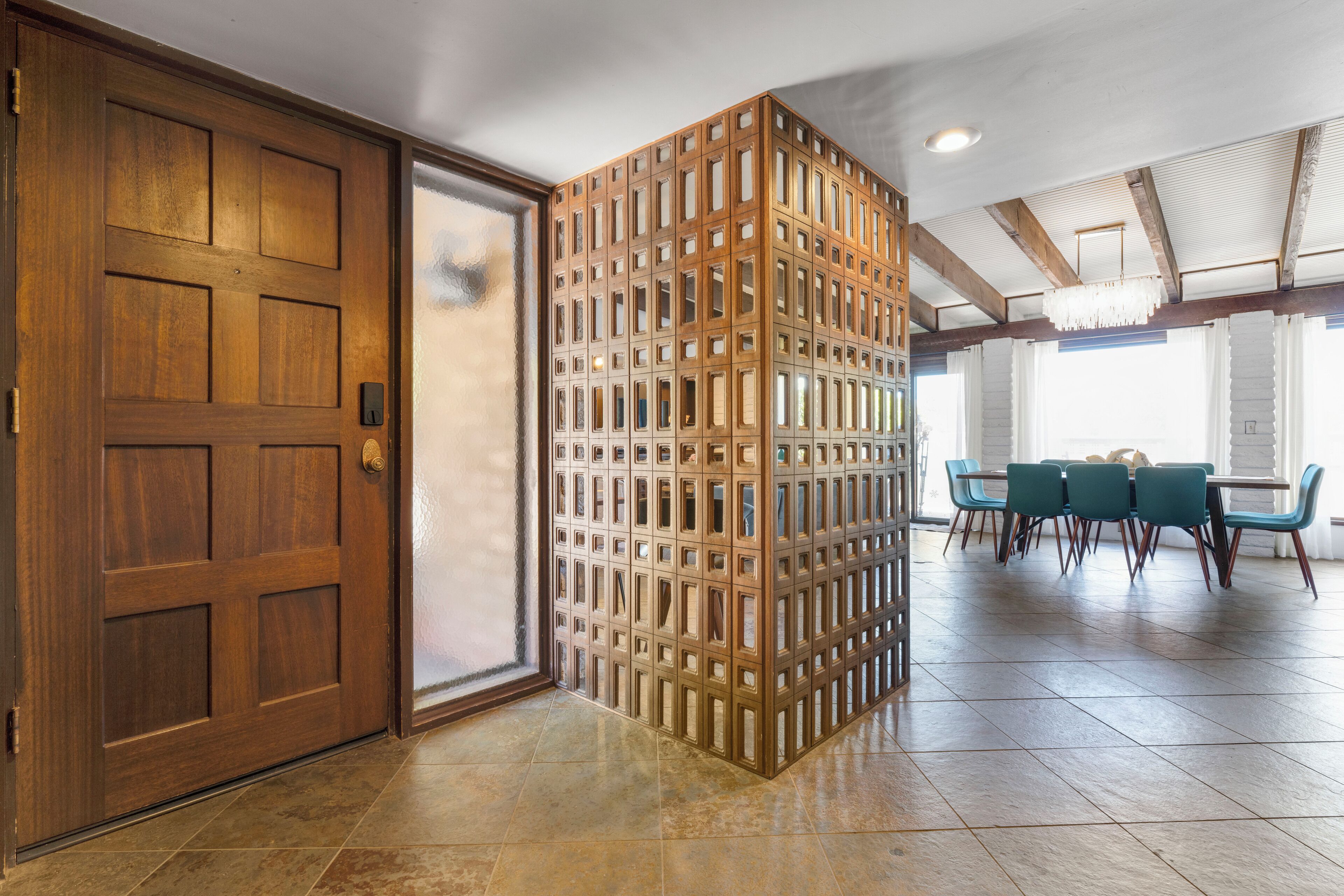 Una stanza con una porta in legno, un tramezzo con diverse piccole finestre, un'area pranzo con tavolo e sedie e un lampadario.