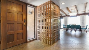 Una habitación con una puerta de madera, un separador con varias ventanas pequeñas, un comedor con mesa y sillas, y un candelabro.