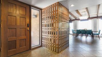 Una stanza con una porta in legno, un tramezzo con diverse piccole finestre, un'area pranzo con tavolo e sedie e un lampadario.