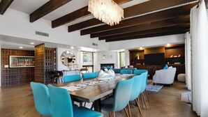 Amplia sala de estar con una gran mesa de comedor de madera rodeada de sillas color turquesa, una chimenea y un televisor al fondo.