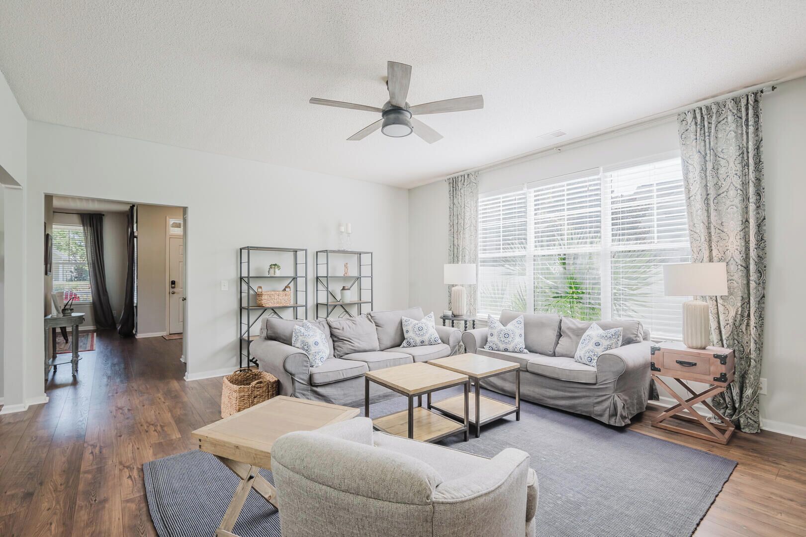 A spacious living room with a large window, a ceiling fan, and a cozy seating area with a sofa and armchairs.