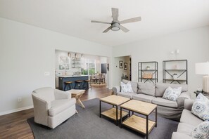 A spacious living room with a sofa, coffee table, and a dining area in the background. - Bluffton Magnolia House (Bluffton)
