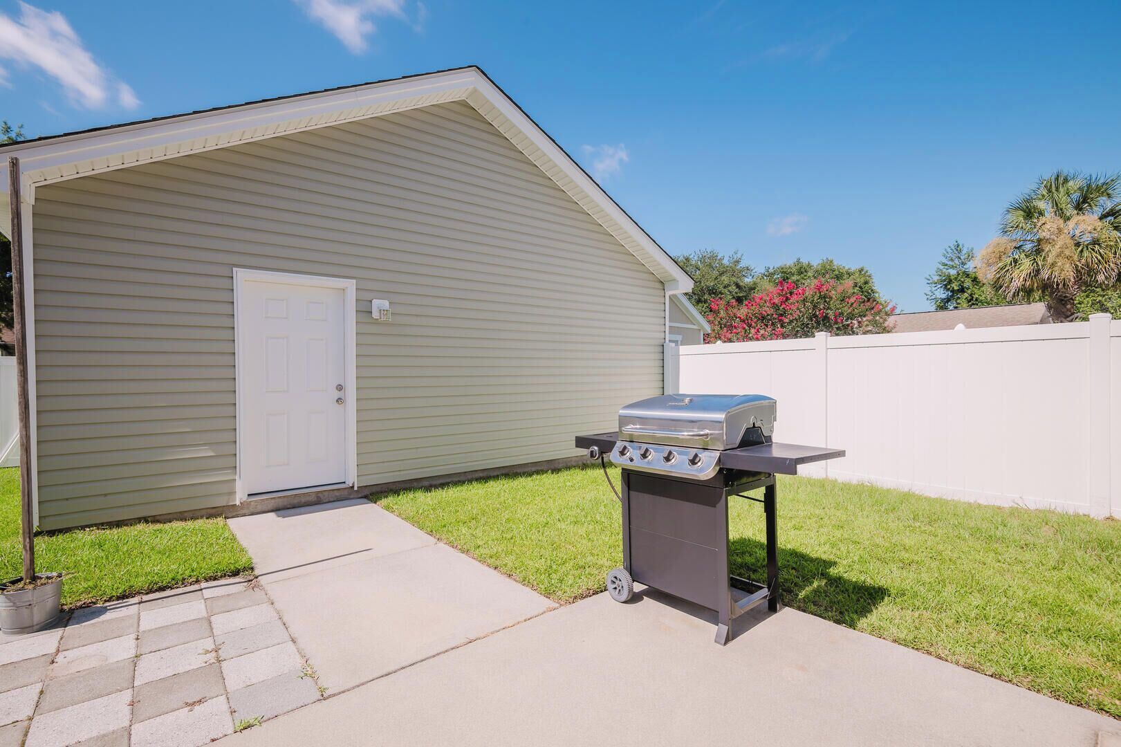 A backyard with a grill set up on a table, a door, and a white fence.