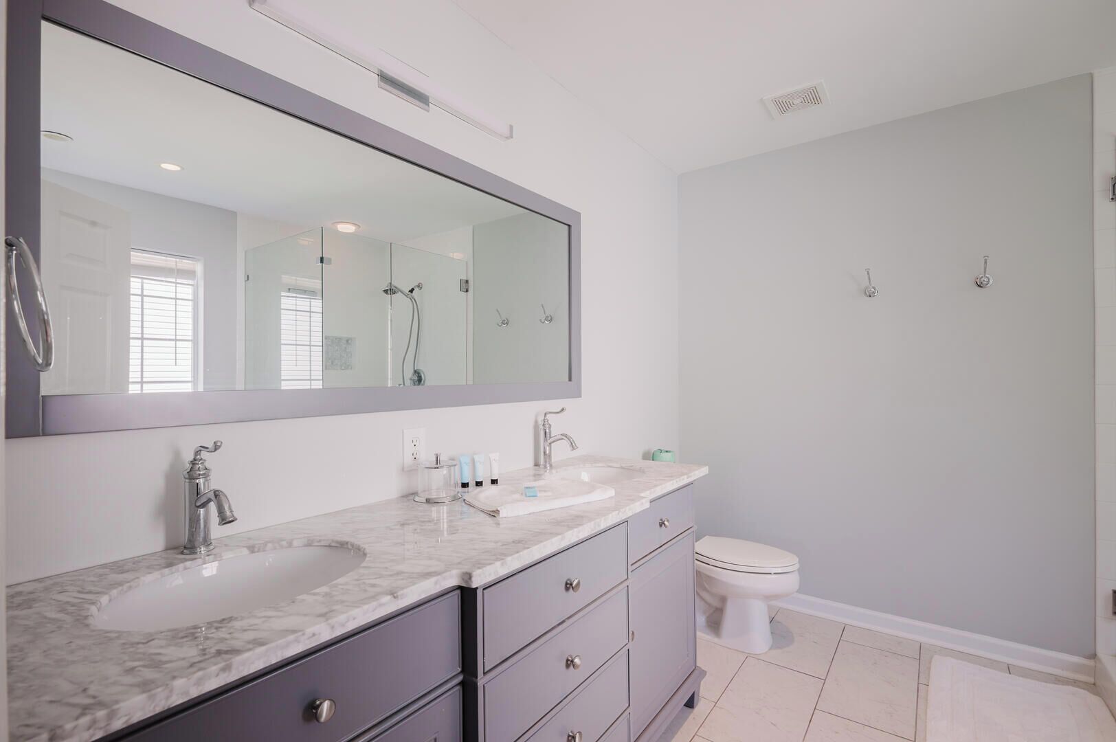 A modern bathroom with a large mirror, two sinks, a toilet, and a shower.