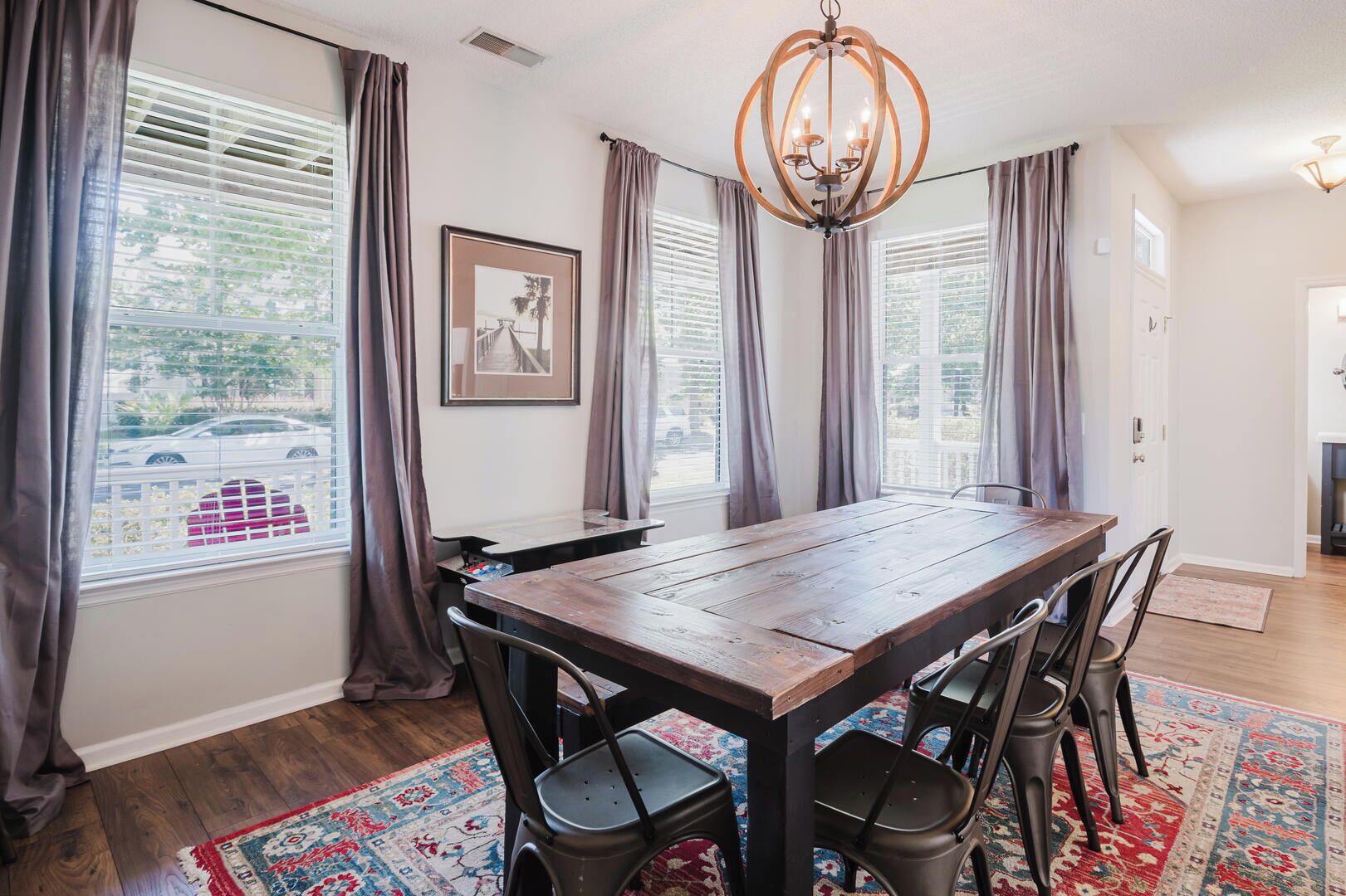 A dining area with a wooden table, four chairs, a chandelier, and a patterned rug.