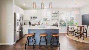A modern kitchen with a central island, bar stools, and a dining area with a table and chairs. - Bluffton Magnolia House (Bluffton)