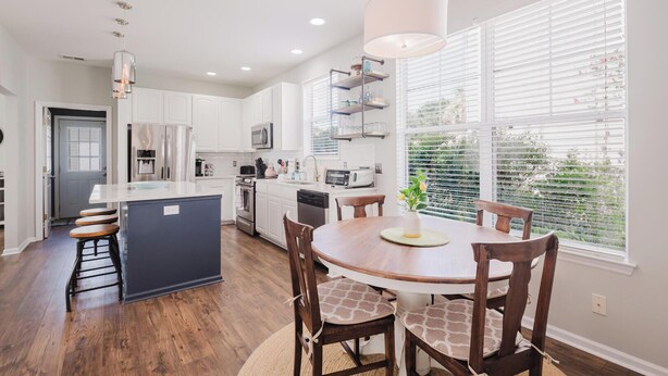 A modern kitchen with white cabinets, a central island, and a dining area with a round table and chairs. - Bluffton Magnolia House (Bluffton)