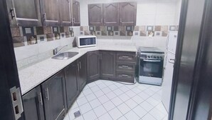 Una cocina compacta con armarios de madera oscura, un microondas blanco, una estufa y un lavamanos.