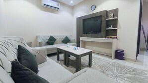 Una sala de estar con sofá, mesa de centro, televisor montado en la pared y aire acondicionado.