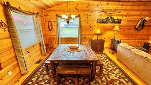 Una habitación acogedora de estilo cabaña con paredes de madera, una mesa con bancos, un sofá y una araña.