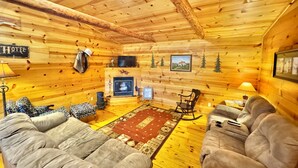 Interior acogedor de una cabaña de troncos con chimenea, dos sofás, un televisor y un cartel que dice 'Hotel'.