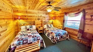 Una habitación de cabaña acogedora con dos camas, un ventilador de techo y una ventana con cortinas.