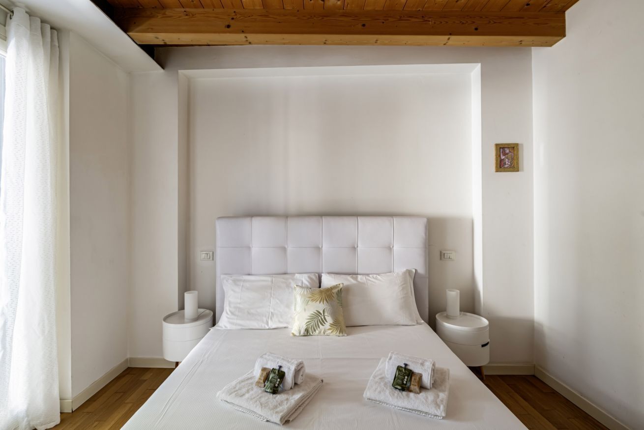 A bedroom with a large bed, two bedside tables, a wooden ceiling, and a white wall.