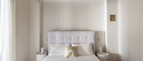 A bedroom with a large bed, two bedside tables, a wooden ceiling, and a white wall.