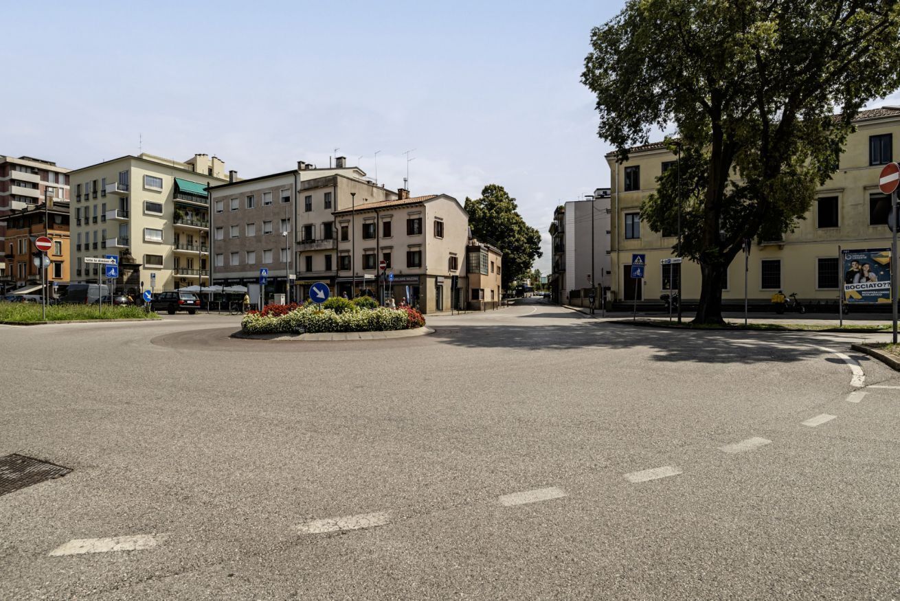 A roundabout with buildings, a tree, and road signs.