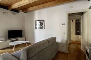 A modern living room with a sofa, a flat-screen TV, a small white table, and a framed picture on the wall.