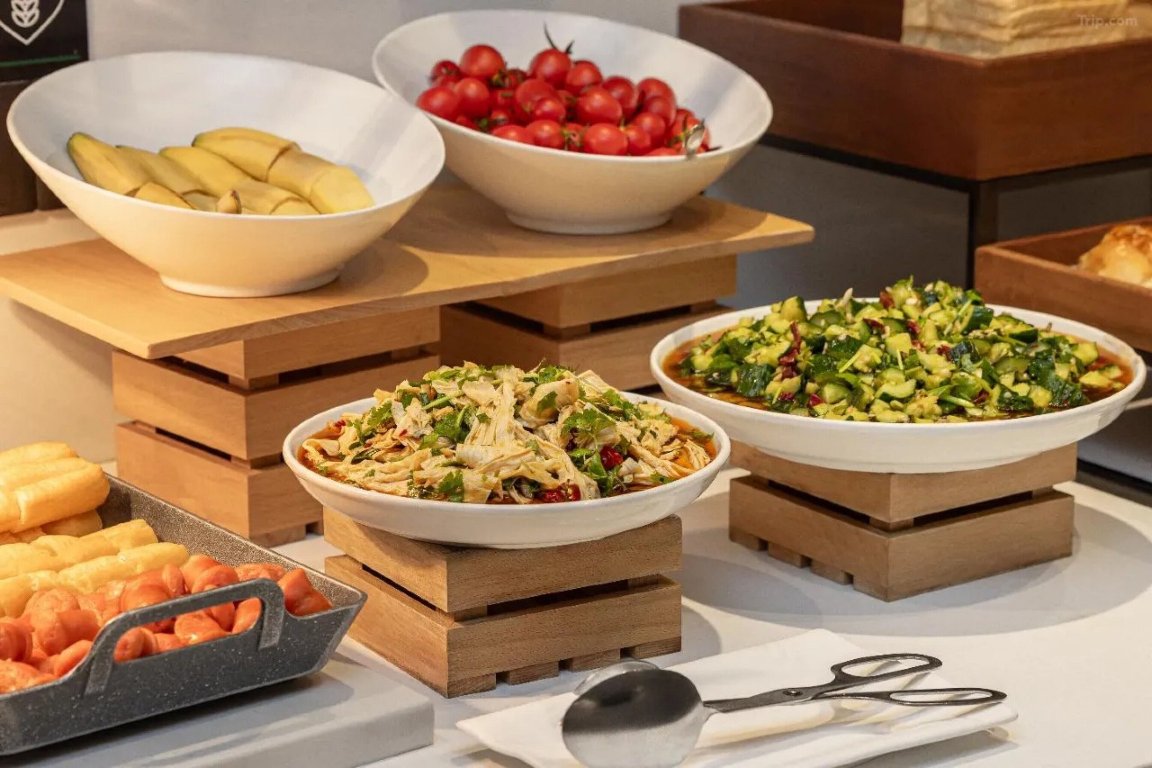 A buffet table with various dishes including sliced bananas, cherry tomatoes, and a salad.
