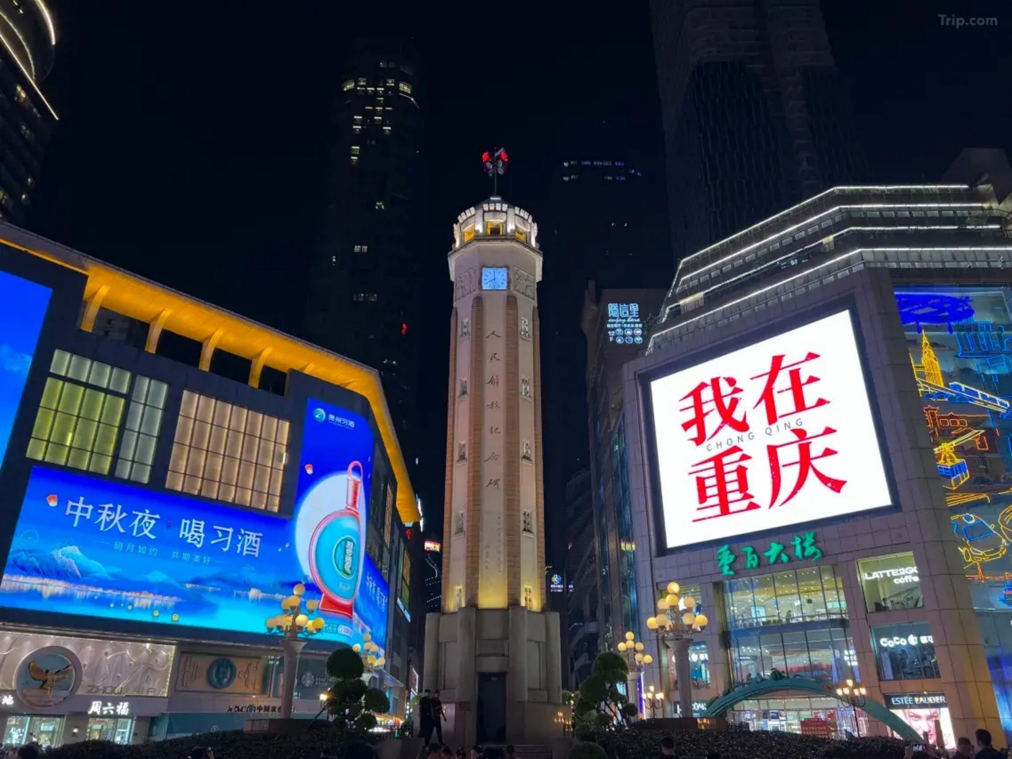 Une vue nocturne d’une ville, avec ses panneaux publicitaires illuminés et un imposant beffroi.