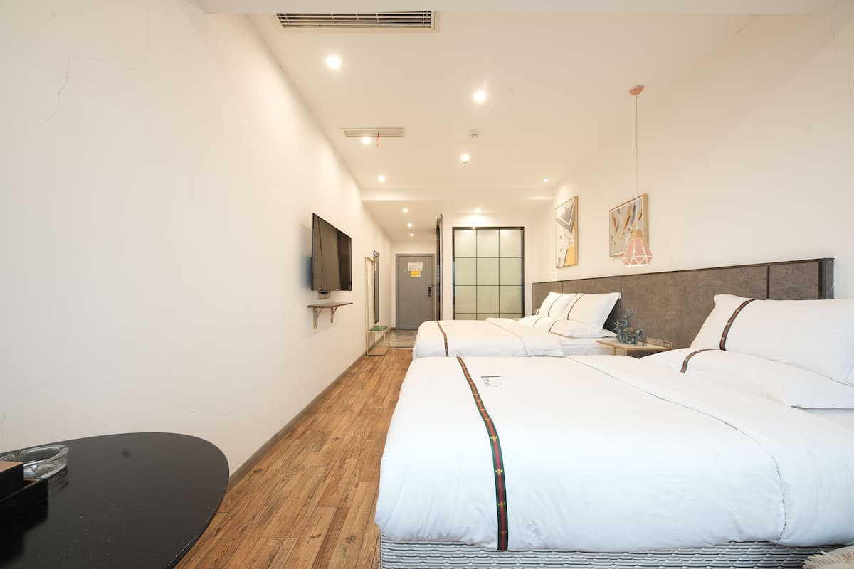 Ein Hotelzimmer mit zwei Betten, einem Flachbildfernseher, Holzboden und einem Flur, der zu einem Badezimmer führt.