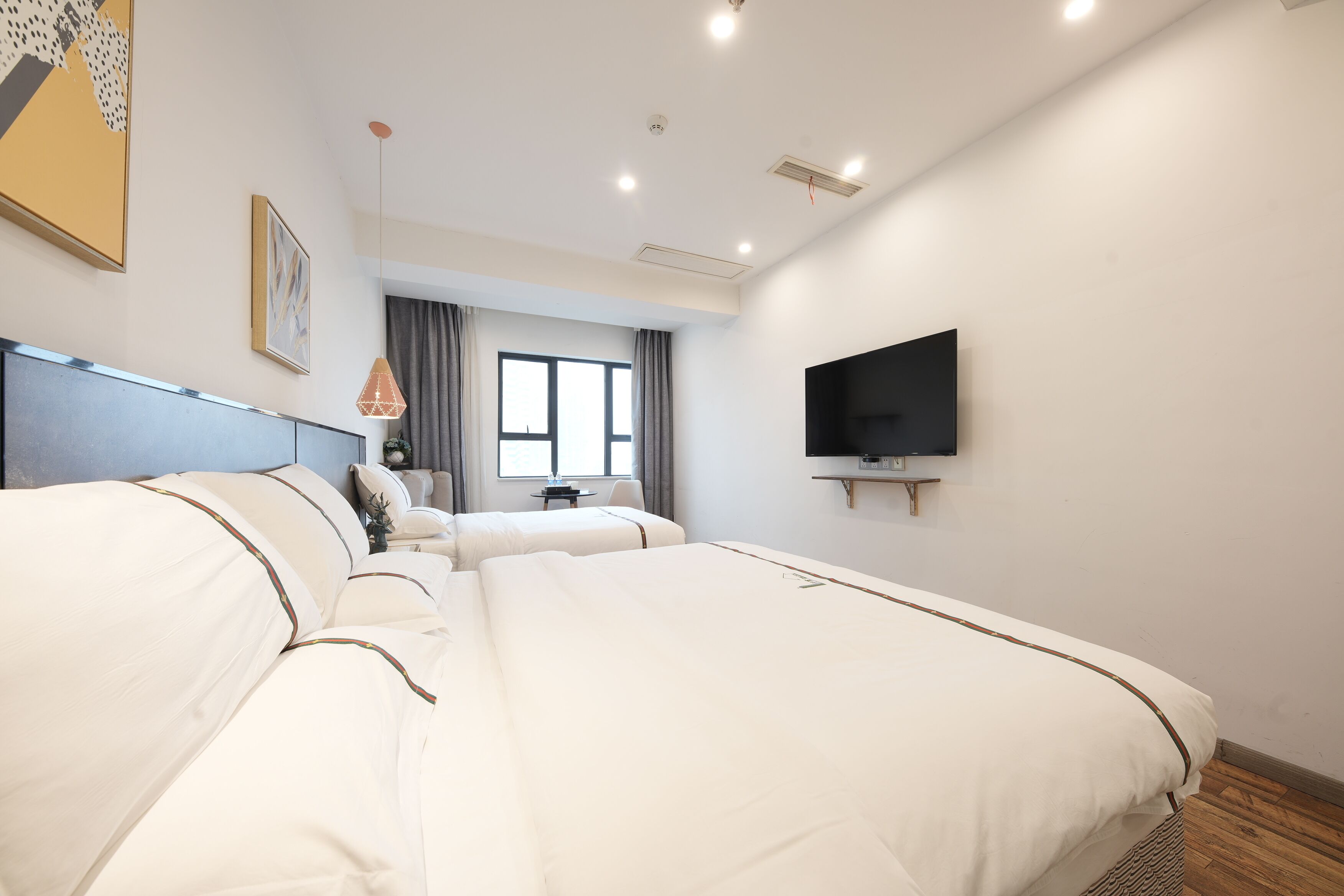 Een hotelkamer met twee bedden, een aan de muur bevestigde televisie en een raam met gordijnen.