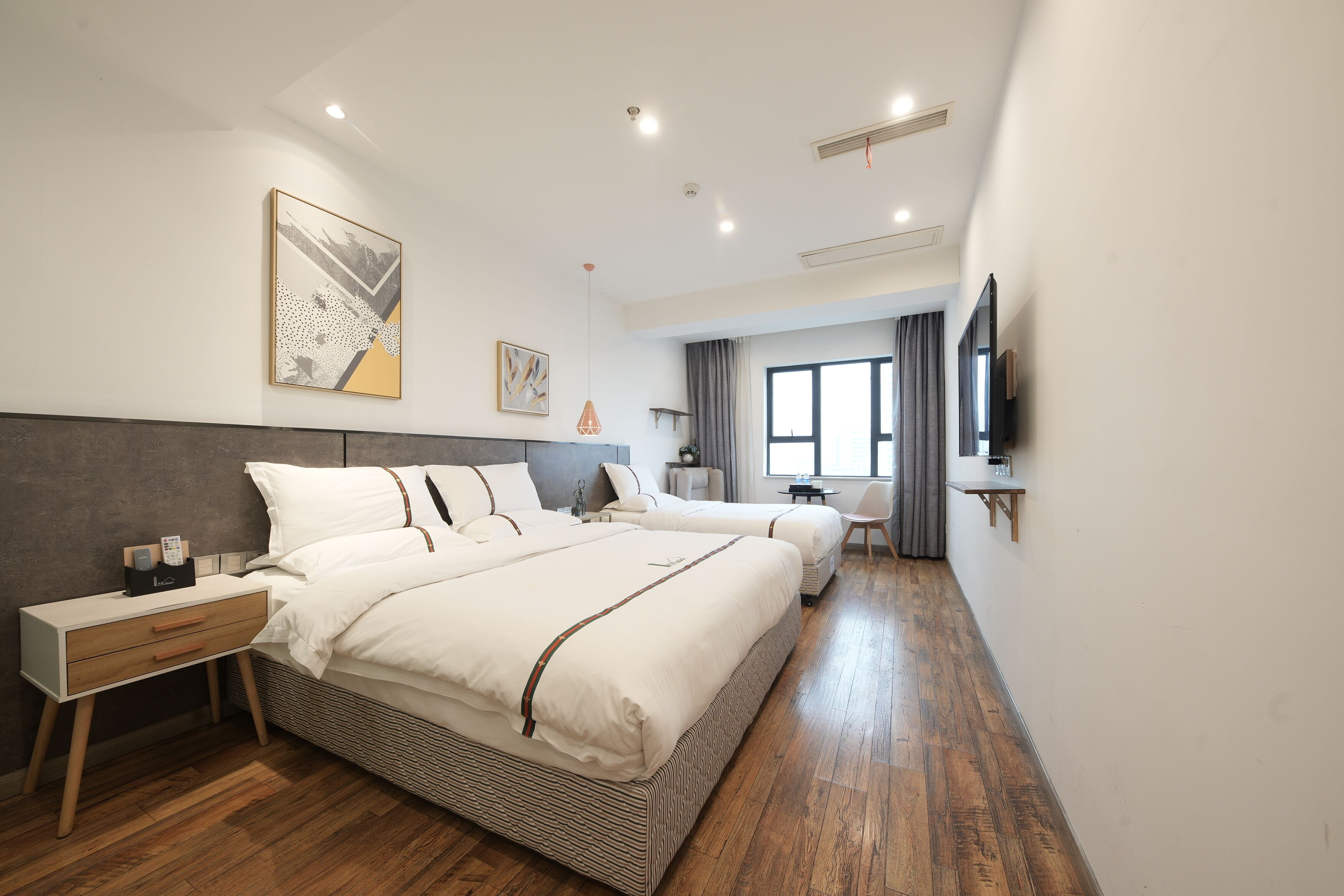 A modern hotel room with a large bed, bedside tables, a TV, and a window with curtains.